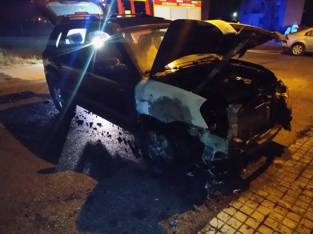 Vehículo calcinado tras un incendio de madrugada en Ponferrada, con bomberos y servicios de emergencia actuando en la zona.