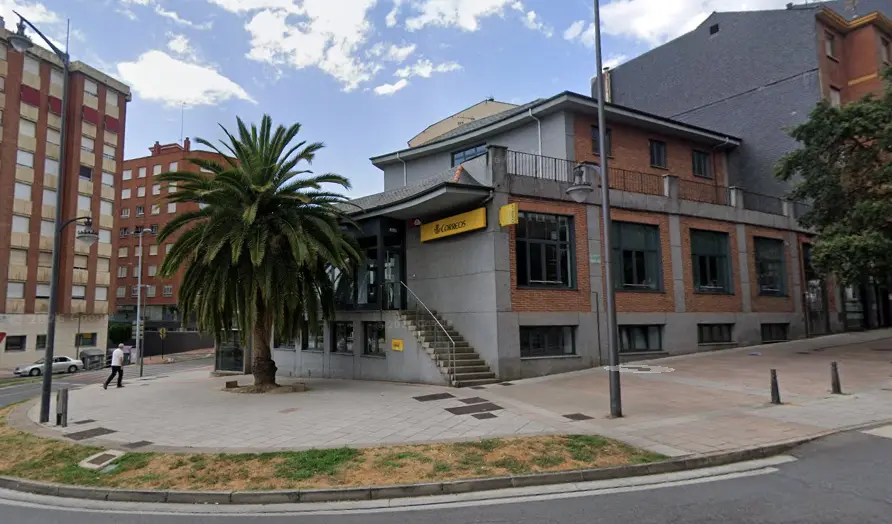 Exterior de la oficina de Correos de Ponferrada, con el edificio de ladrillo y una palmera junto al acceso principal.