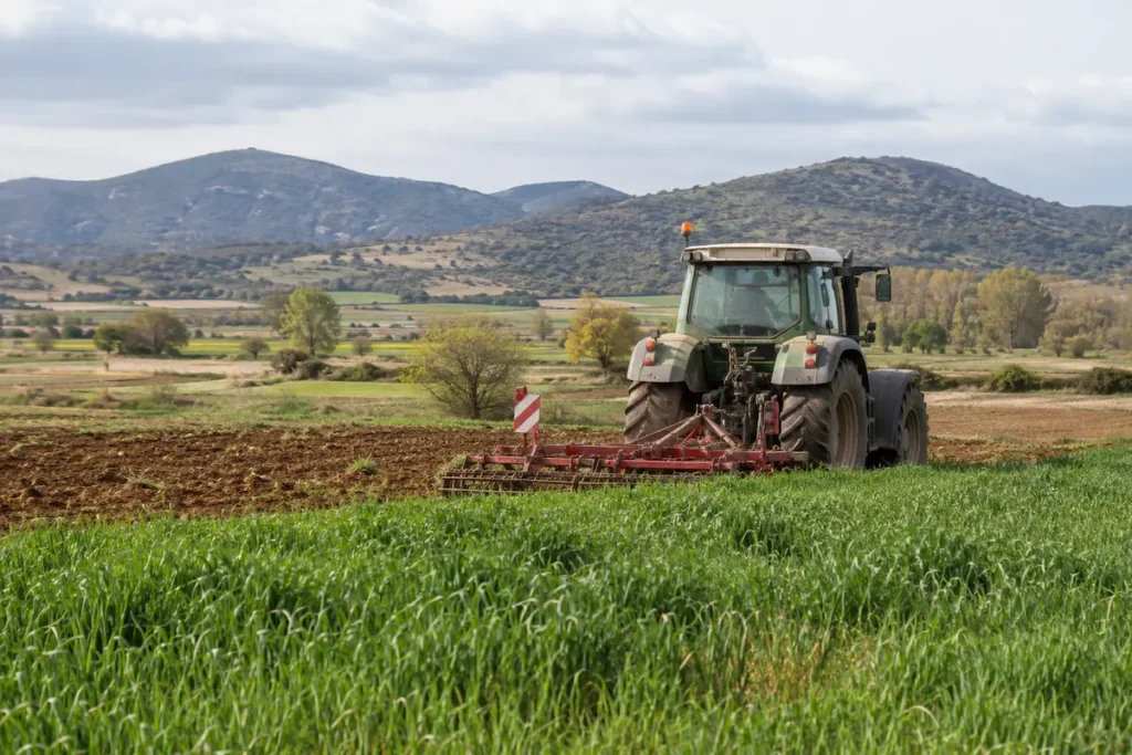 Tractor trabajando en una finca agrícola con montañas al fondo, imagen representativa del campo en la provincia de León.
