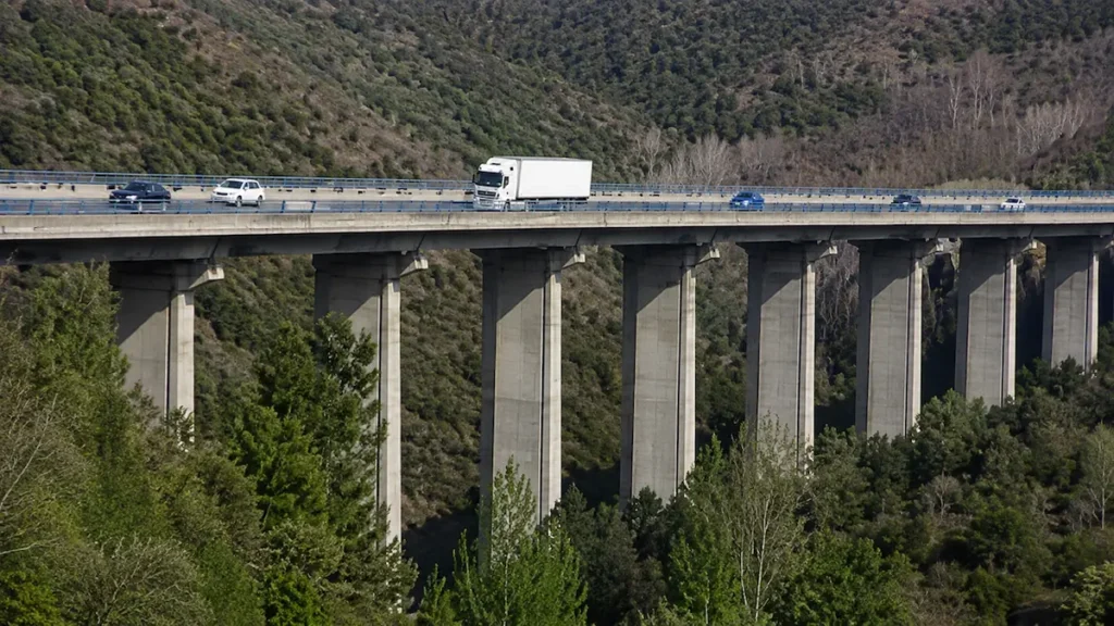 Vehículos circulando por un viaducto de la A-6 sobre un valle arbolado