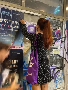 Mujer colocando un cartel morado contra la violencia machista en una pared de Ponferrada